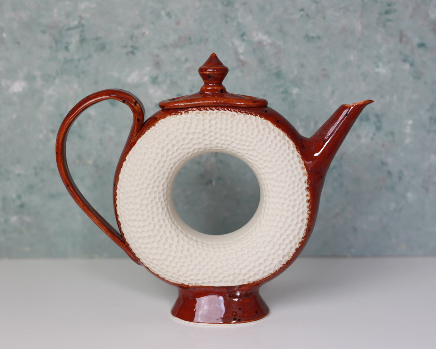 Red ceramic teapot with a white circular design on a textured gray background