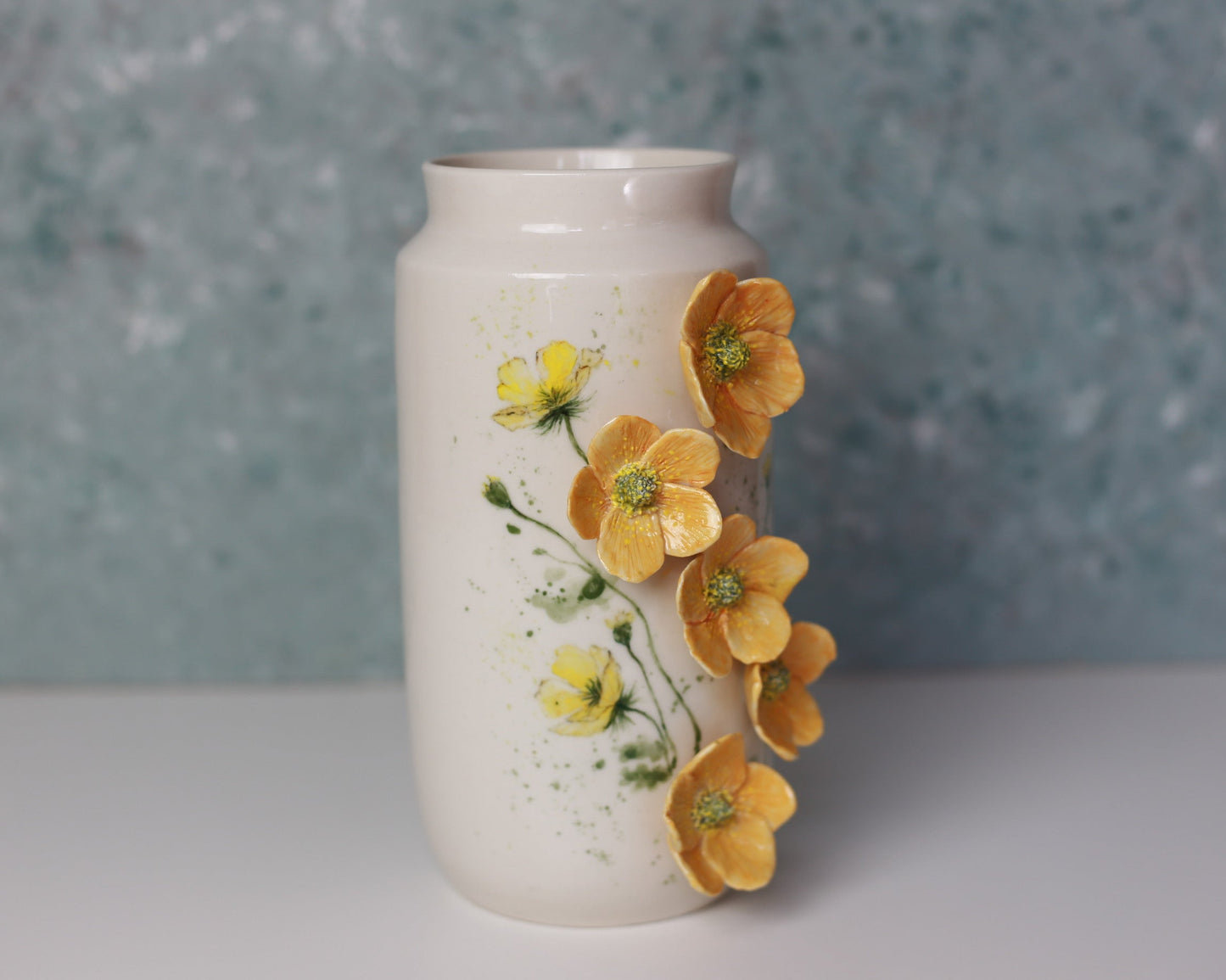 White ceramic vase with yellow floral decorations on a textured blue background