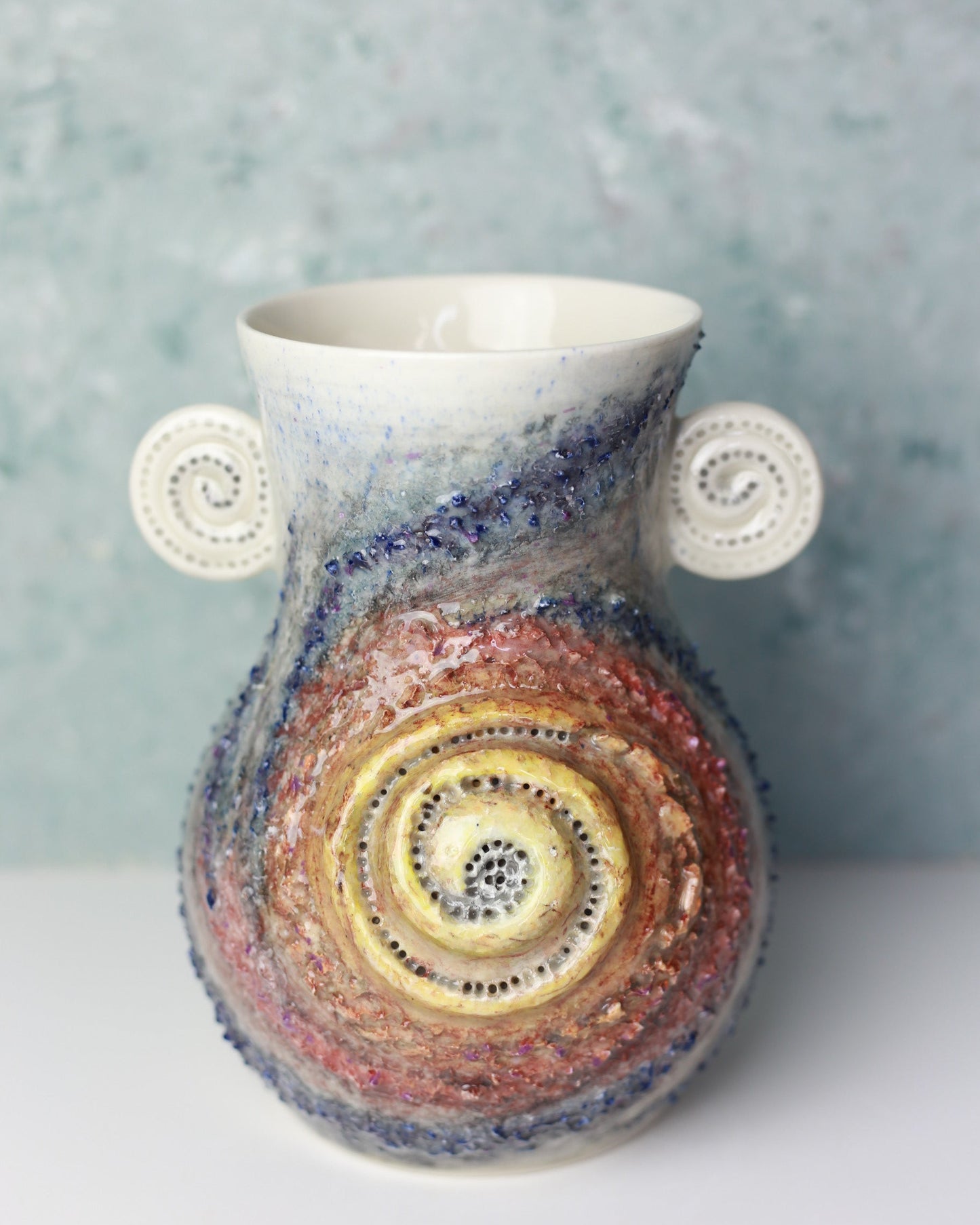 Colorful ceramic vase with spiral design on a textured surface