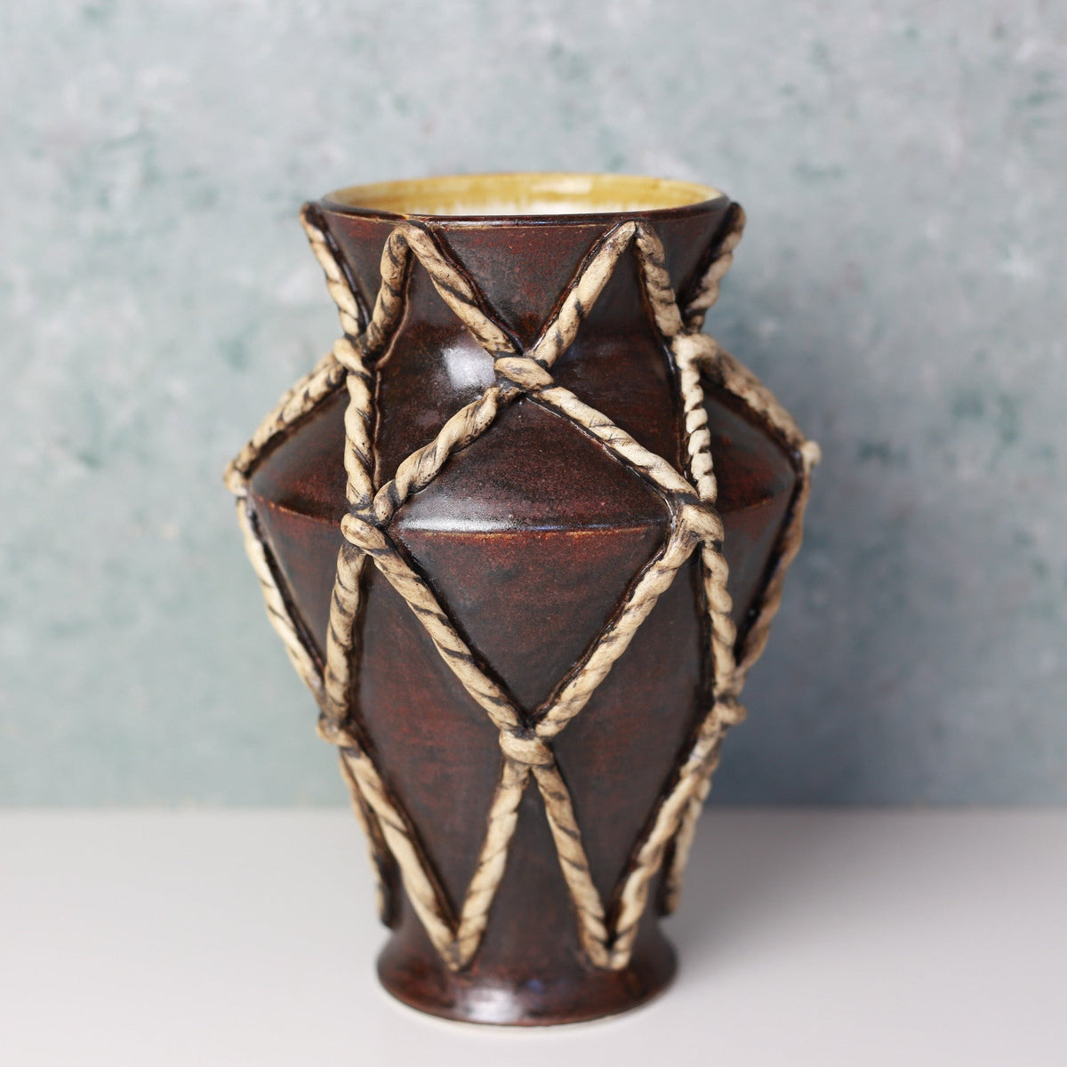 Brown ceramic vase with rope design on a gray background