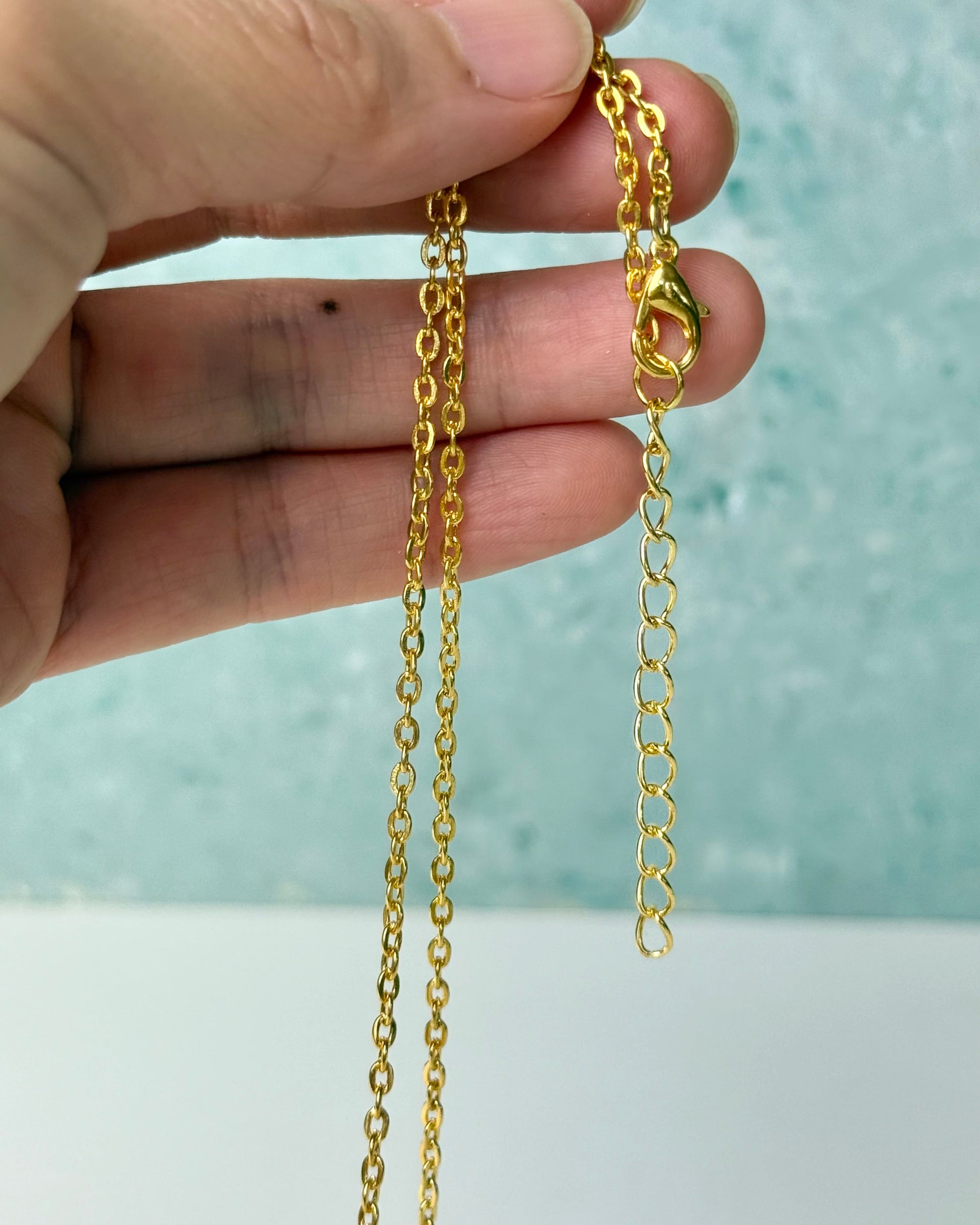 Gold chain held between fingers against a light background