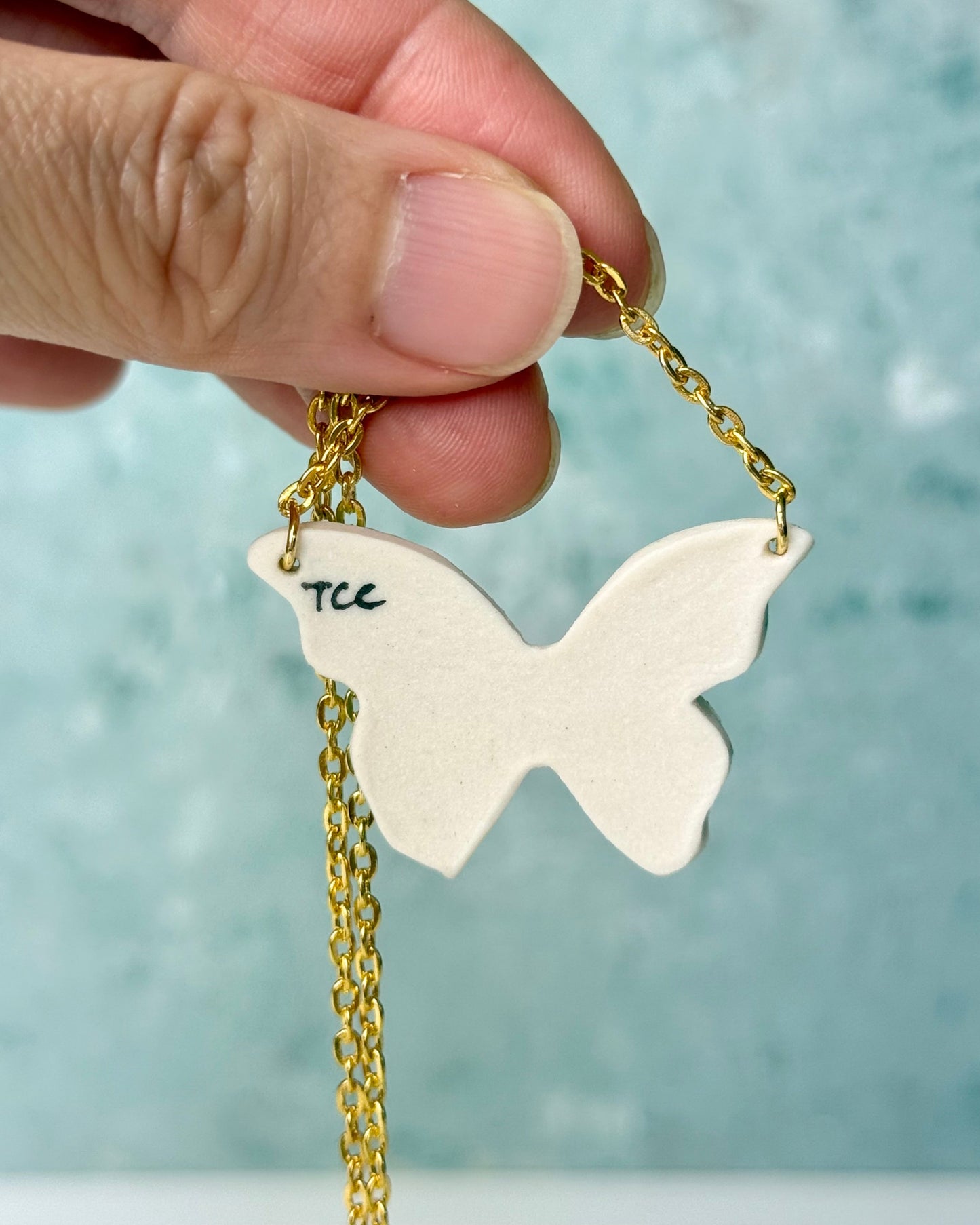 Butterfly-shaped pendant with gold chain held by a hand against a light blue background