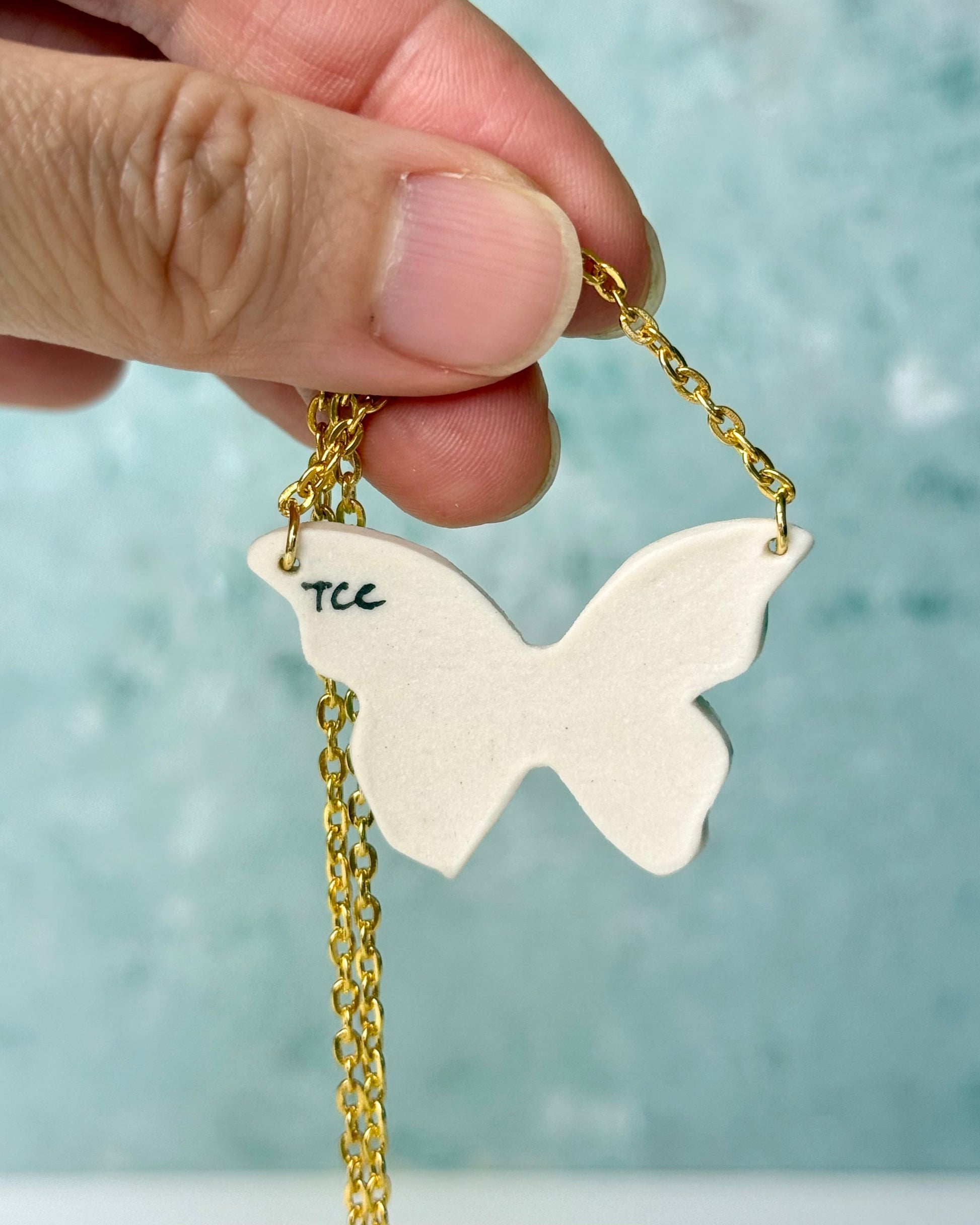 Butterfly-shaped pendant with gold chain held by a hand against a light blue background