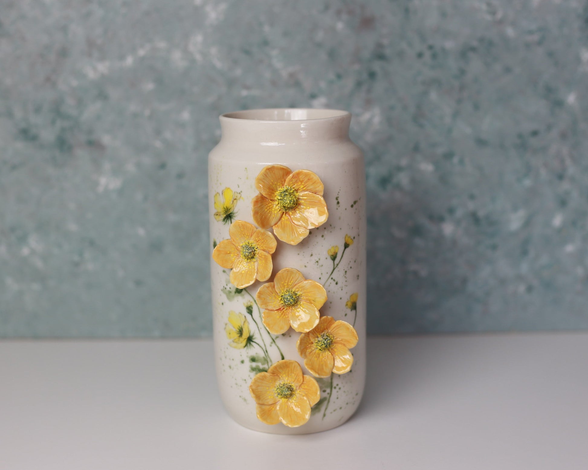 Cylindrical ceramic vase with yellow floral design on a textured blue background