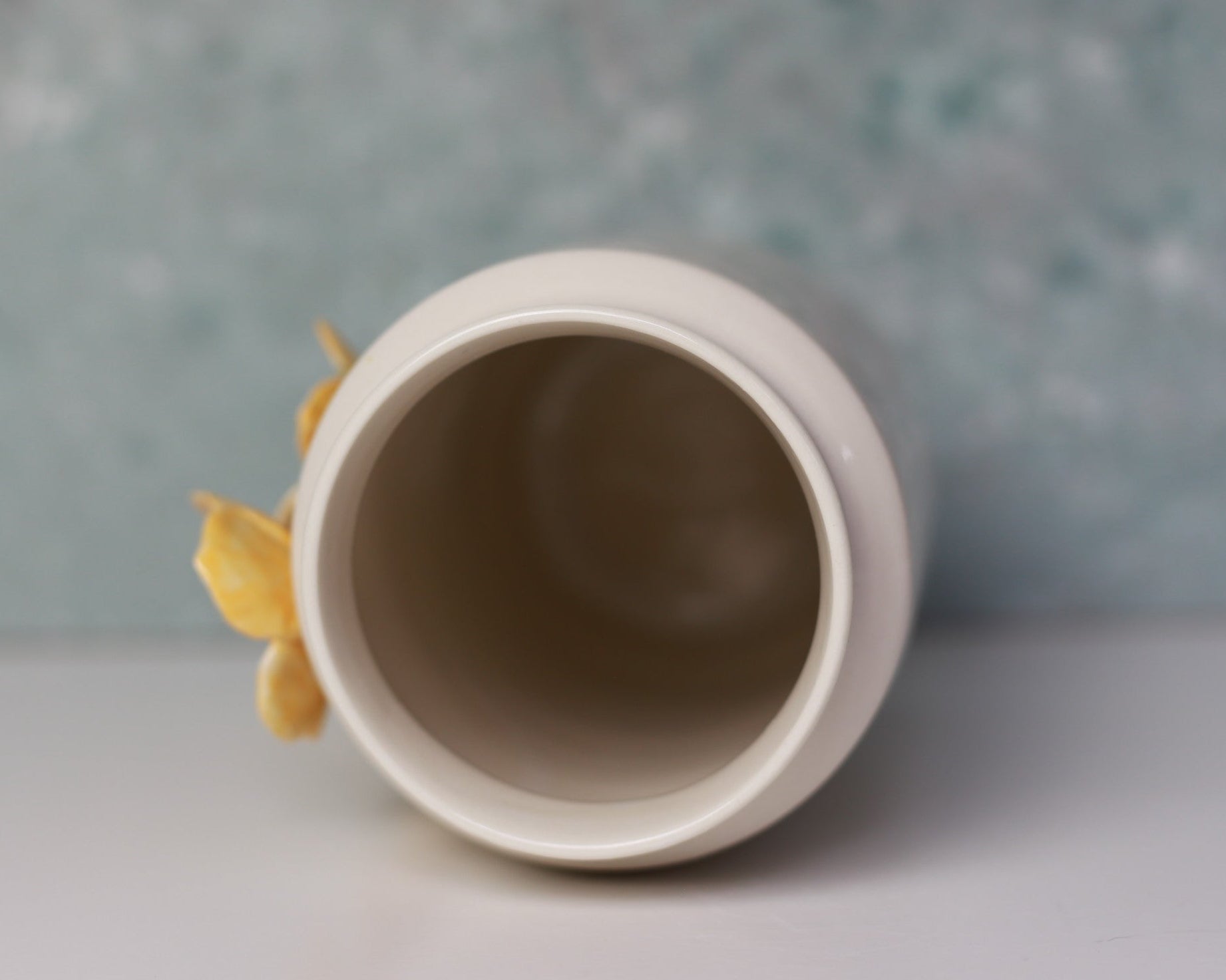 Ceramic vase with a yellow flower on a textured gray background
