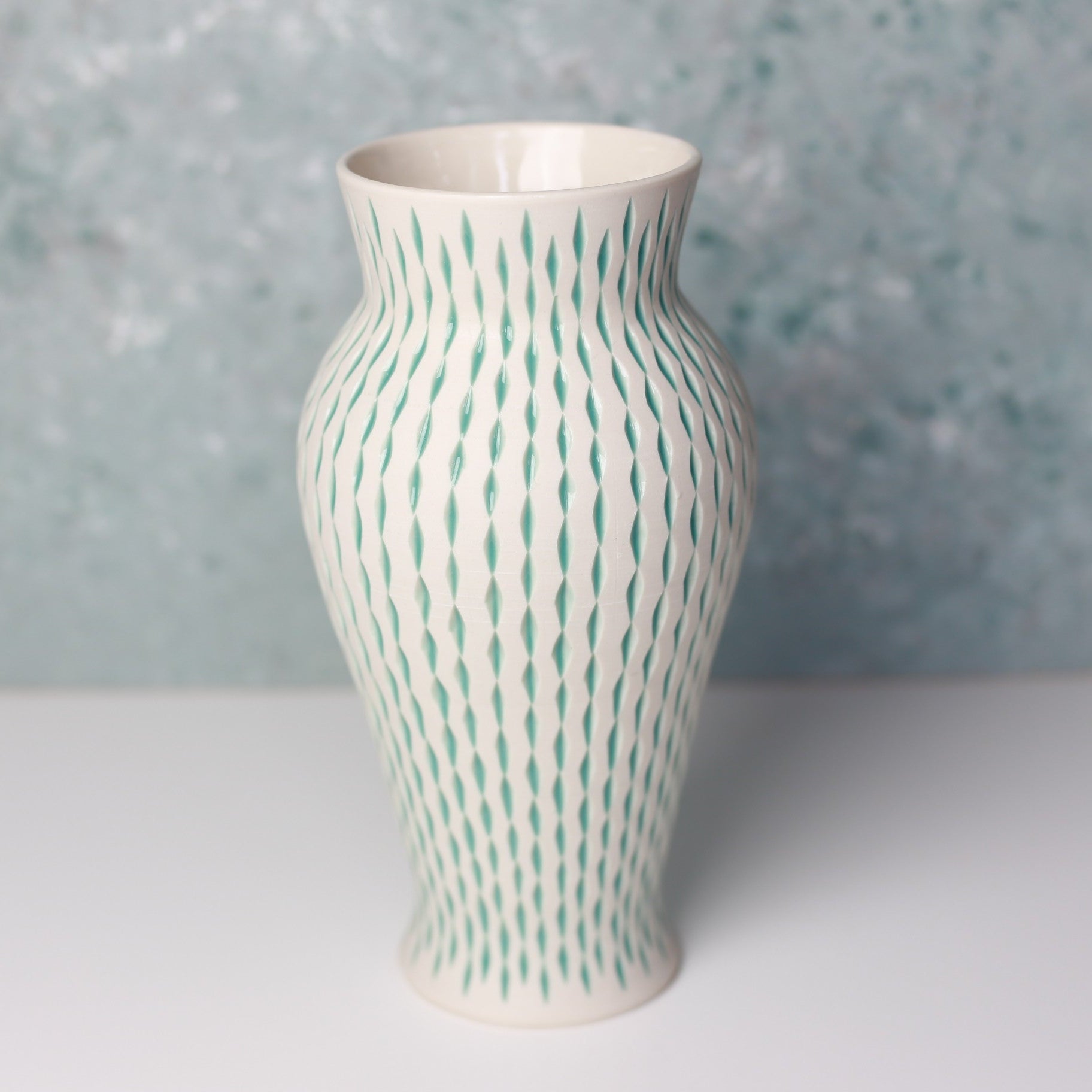 Ceramic vase with green pattern on a light gray surface and blue speckled background