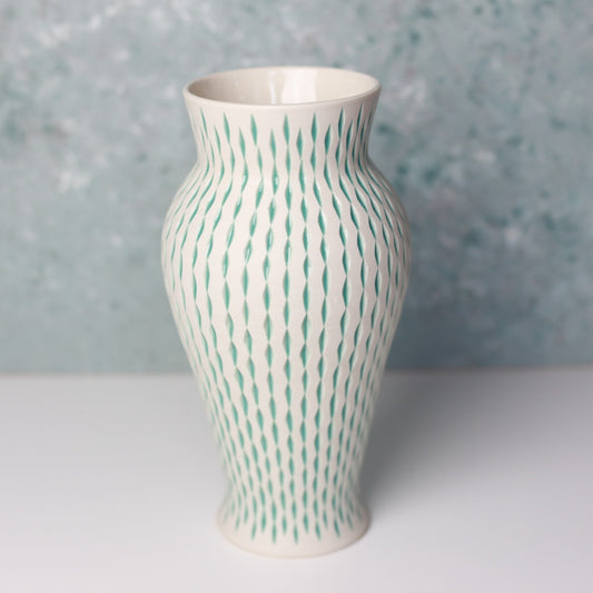 Ceramic vase with green pattern on a light gray surface and blue speckled background