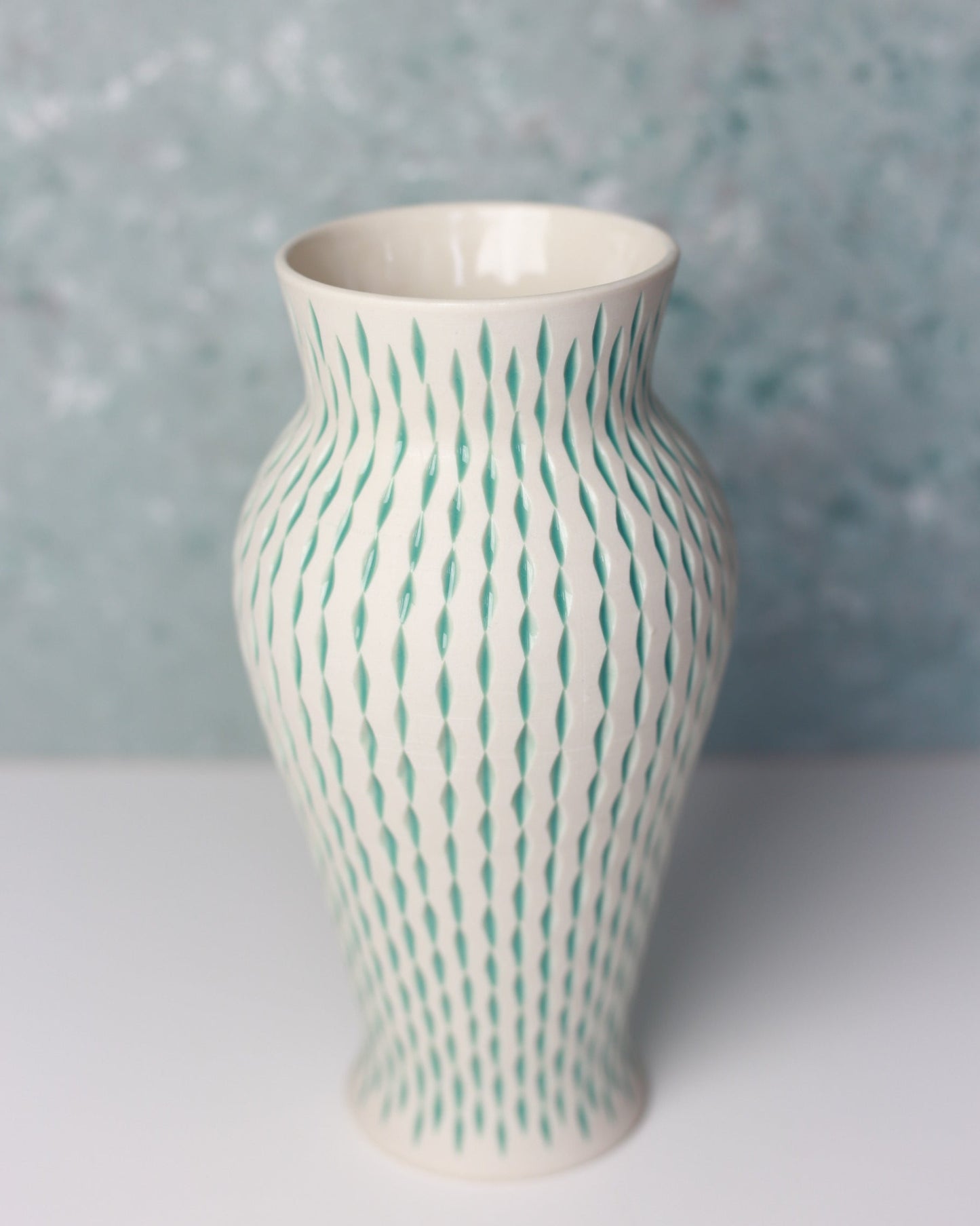 White vase with green wavy pattern on a textured gray background