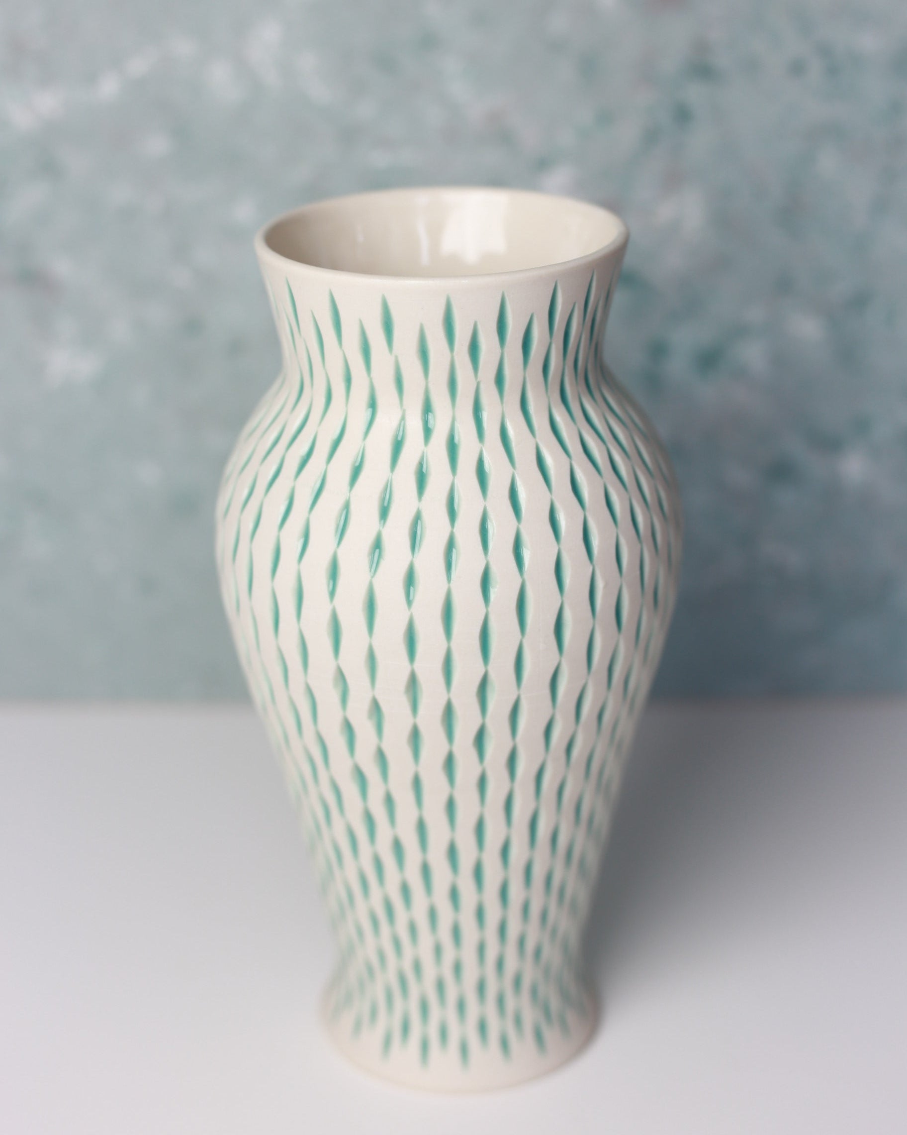White vase with green wavy pattern on a textured gray background