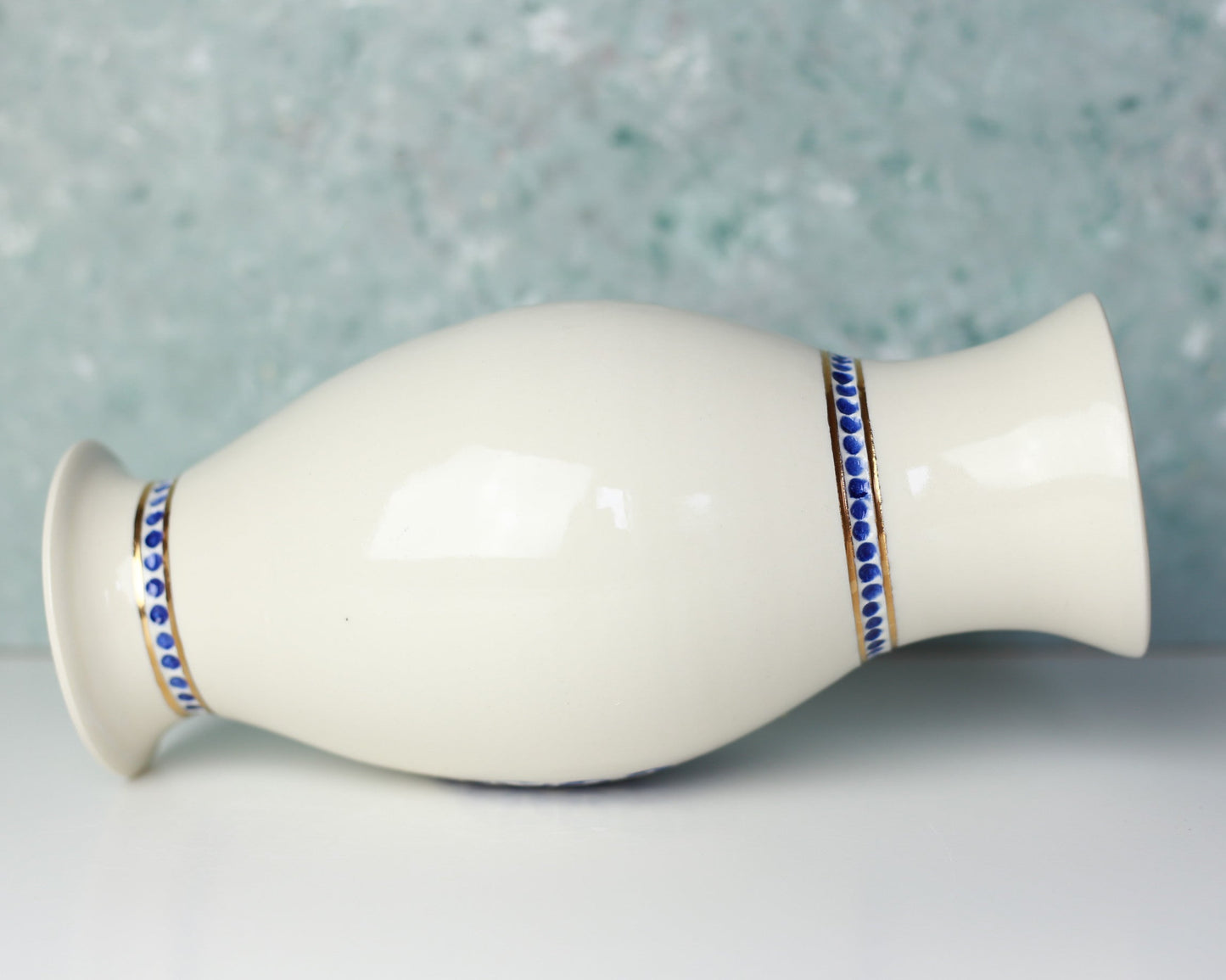 White ceramic vase with blue and gold decorative band on a light gray background
