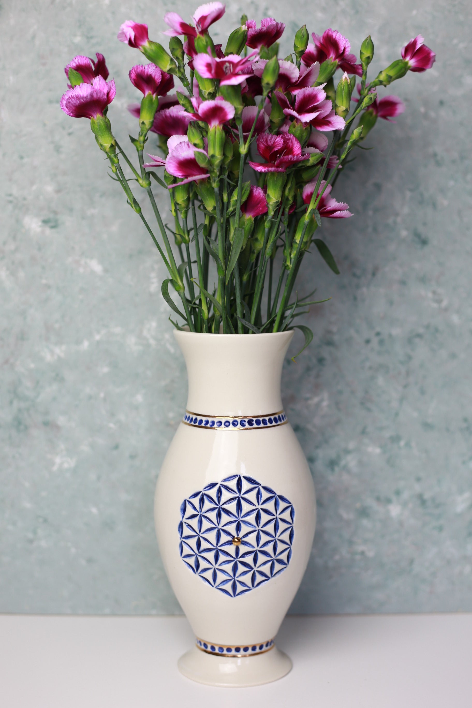 Decorative vase with geometric design holding pink flowers against a light gray background