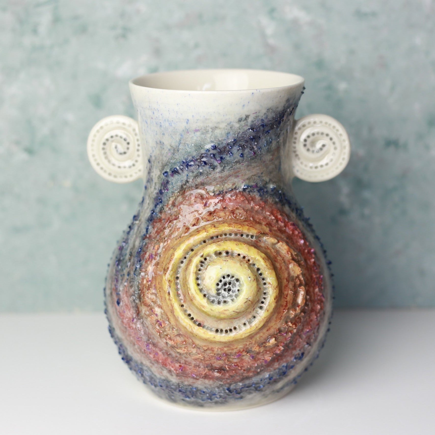 Ceramic vase with multicolored spiral design on a textured gray background
