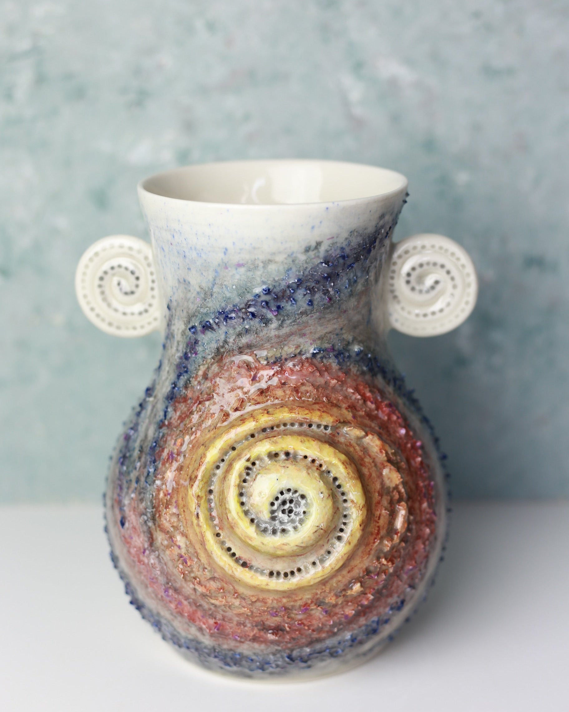 Colorful ceramic vase with spiral design on a textured surface