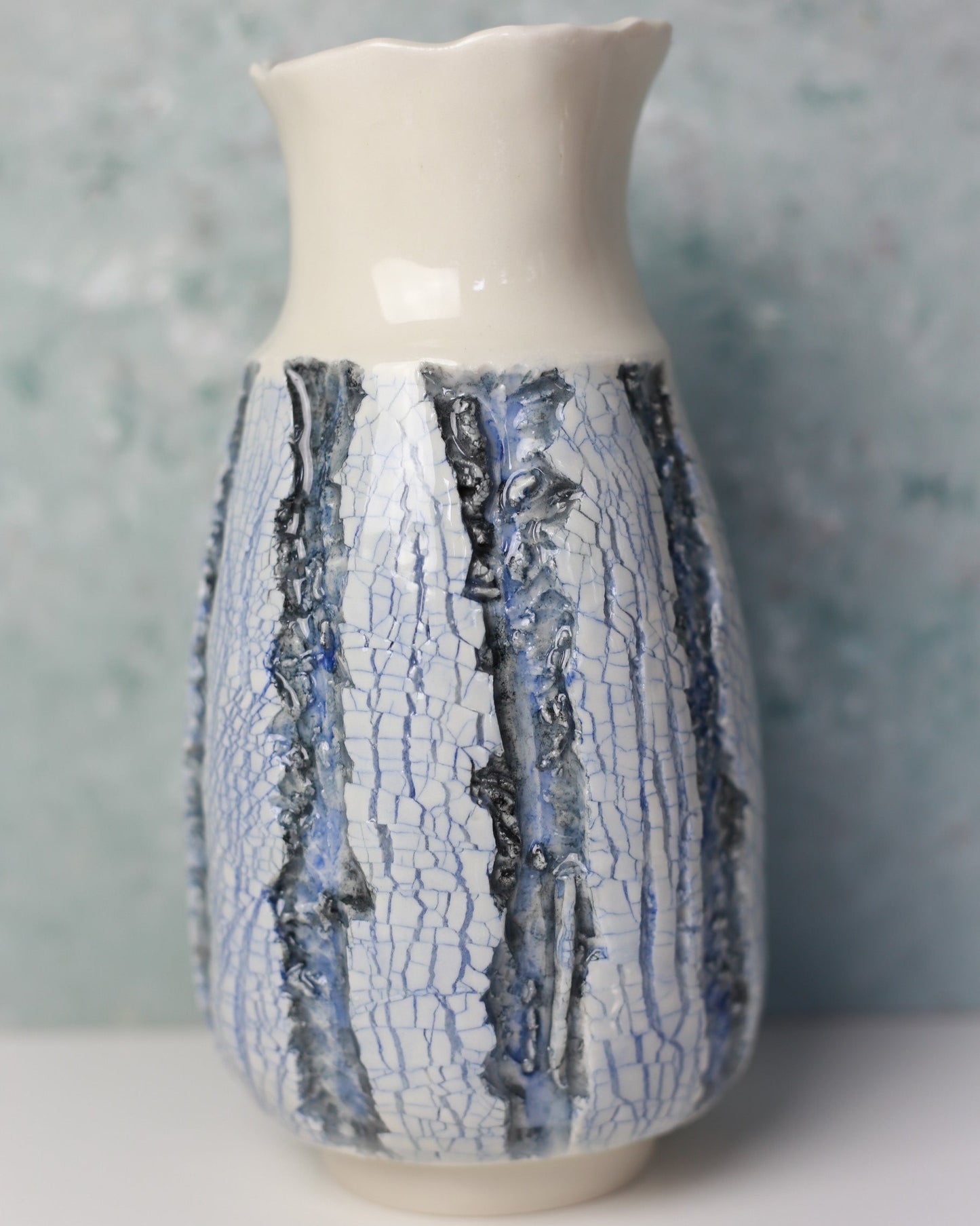 Ceramic vase with white base and blue crackle glaze on a gray background