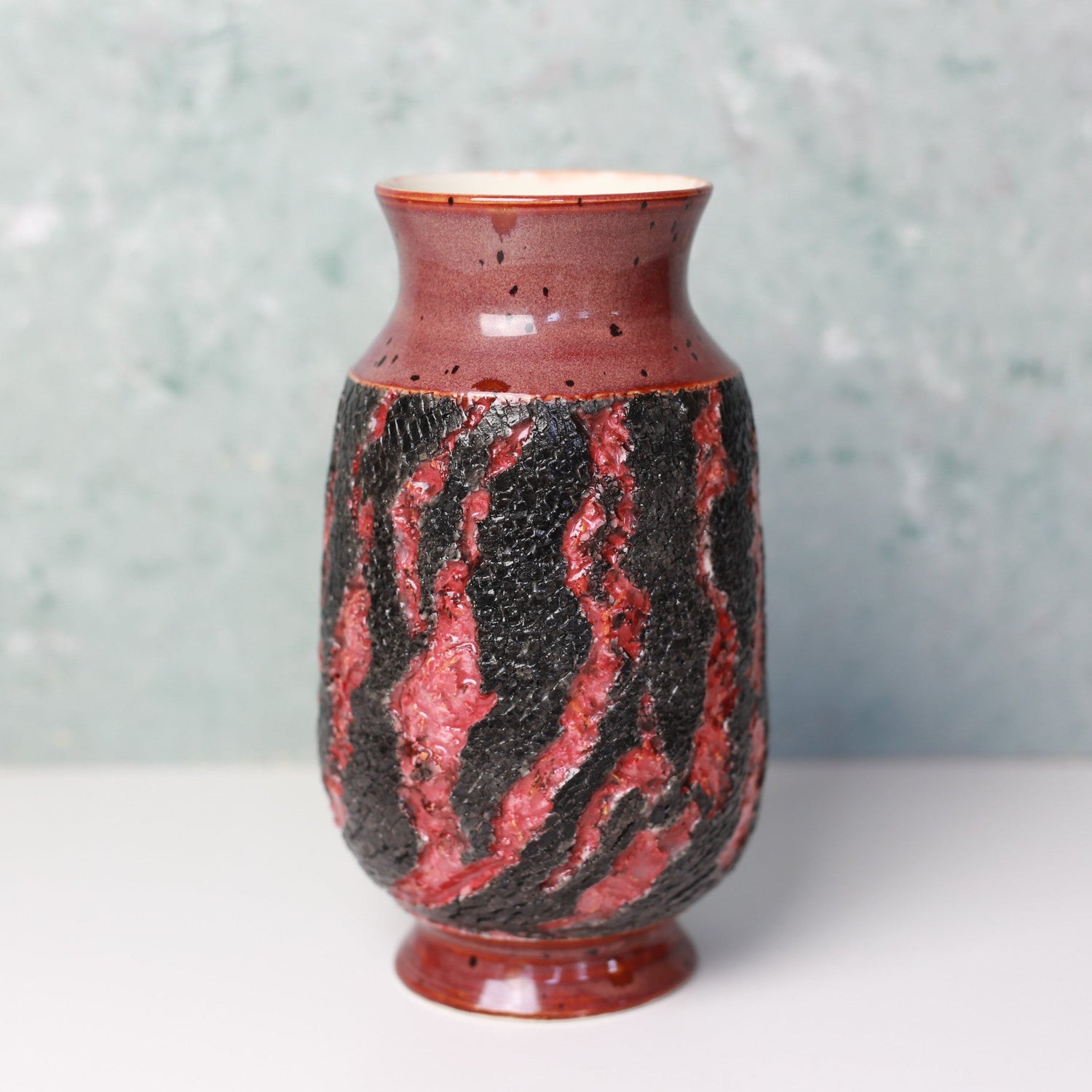 Ceramic vase with red and black pattern on a light gray background