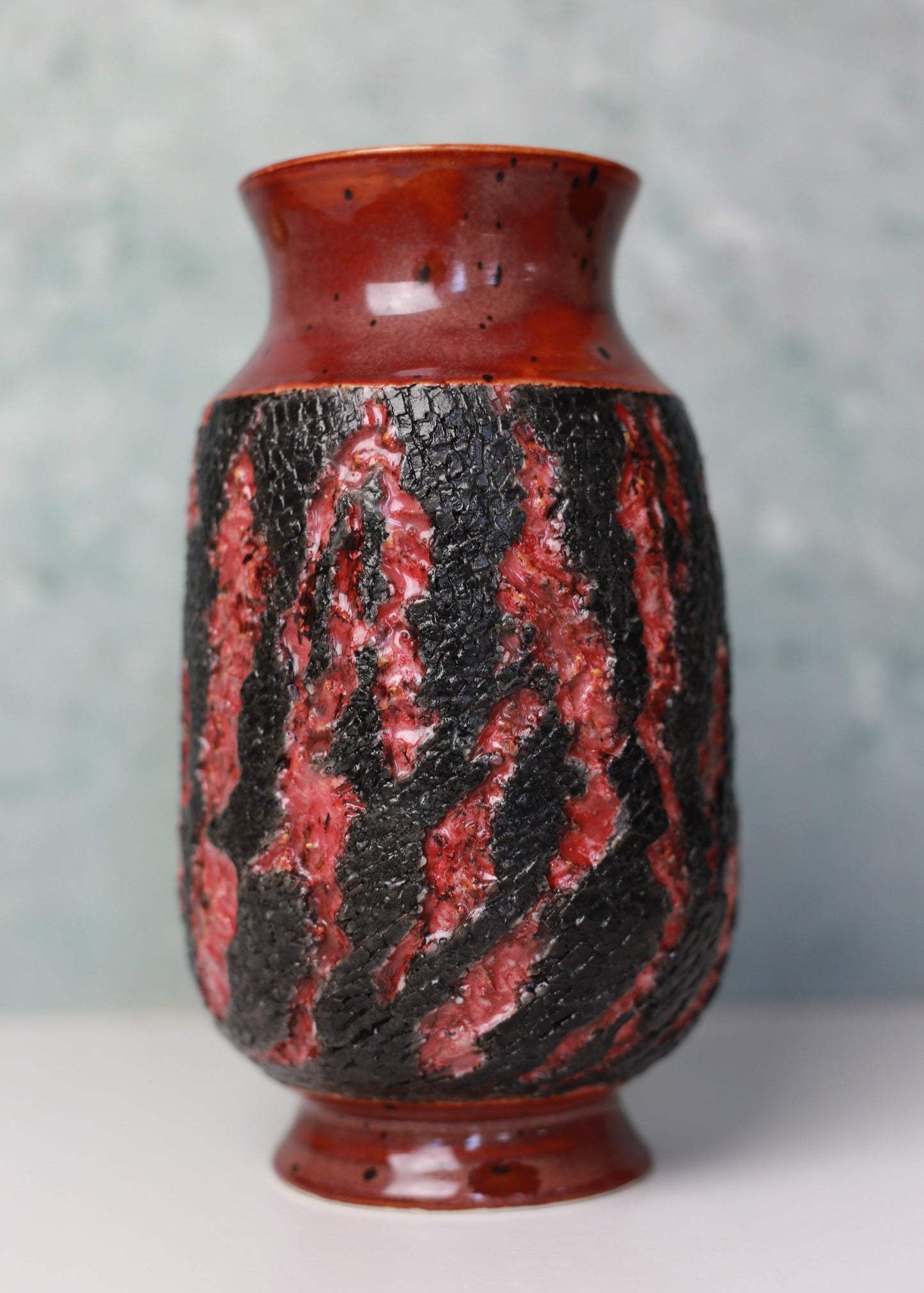 Ceramic vase with red and black pattern on a textured gray background