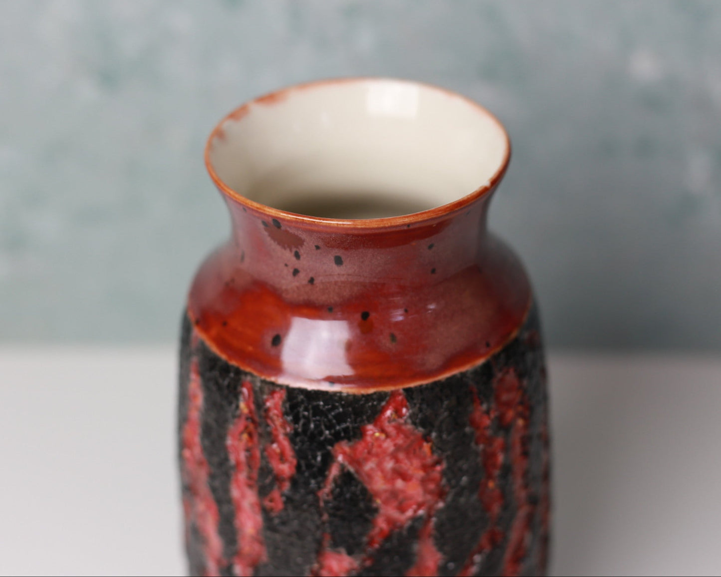 Red and black ceramic vase on a white surface with a gray background