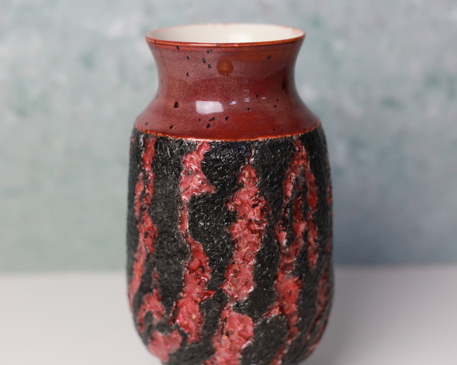 Ceramic vase with red and black pattern on a white surface with a gray background