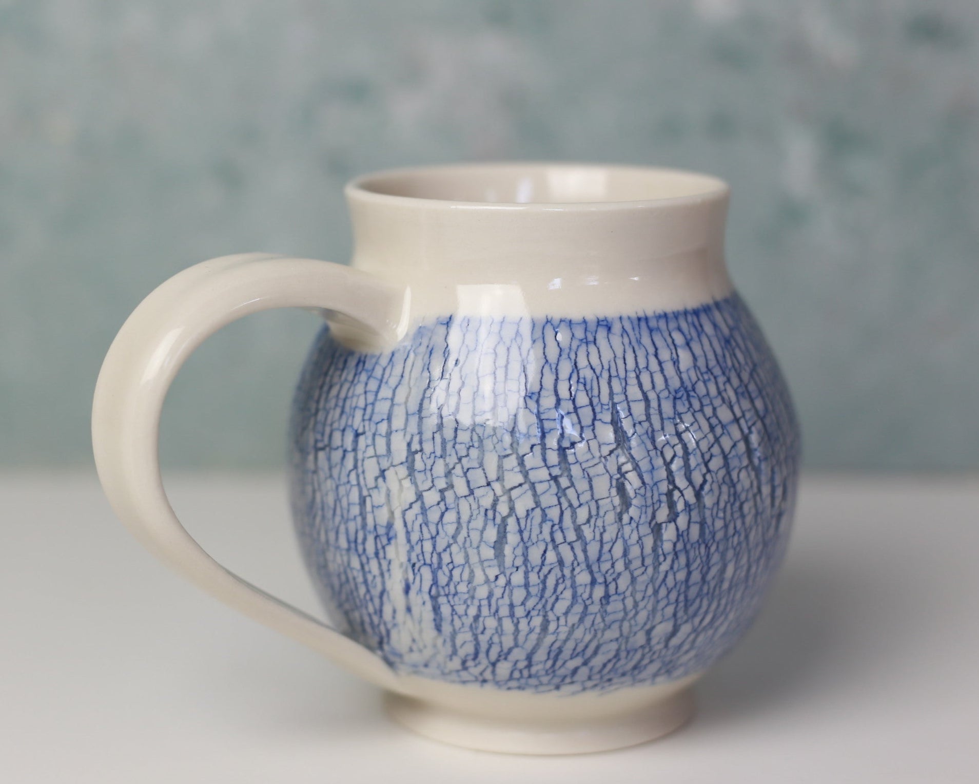Ceramic mug with blue cracked pattern on a white surface and gray background