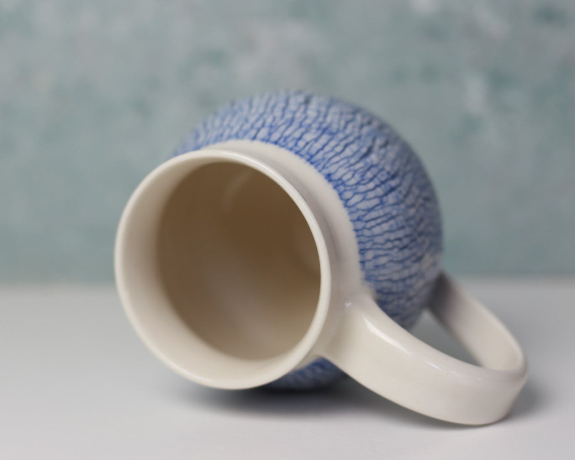 Ceramic mug with textured blue exterior and white interior on a gray background