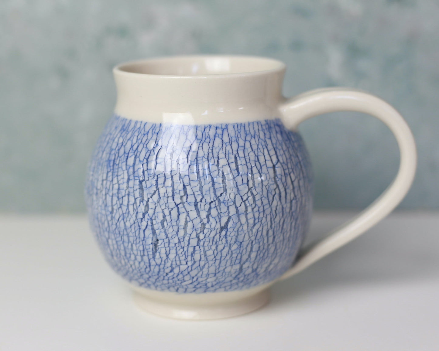 Ceramic mug with blue textured pattern on a white surface with a gray background