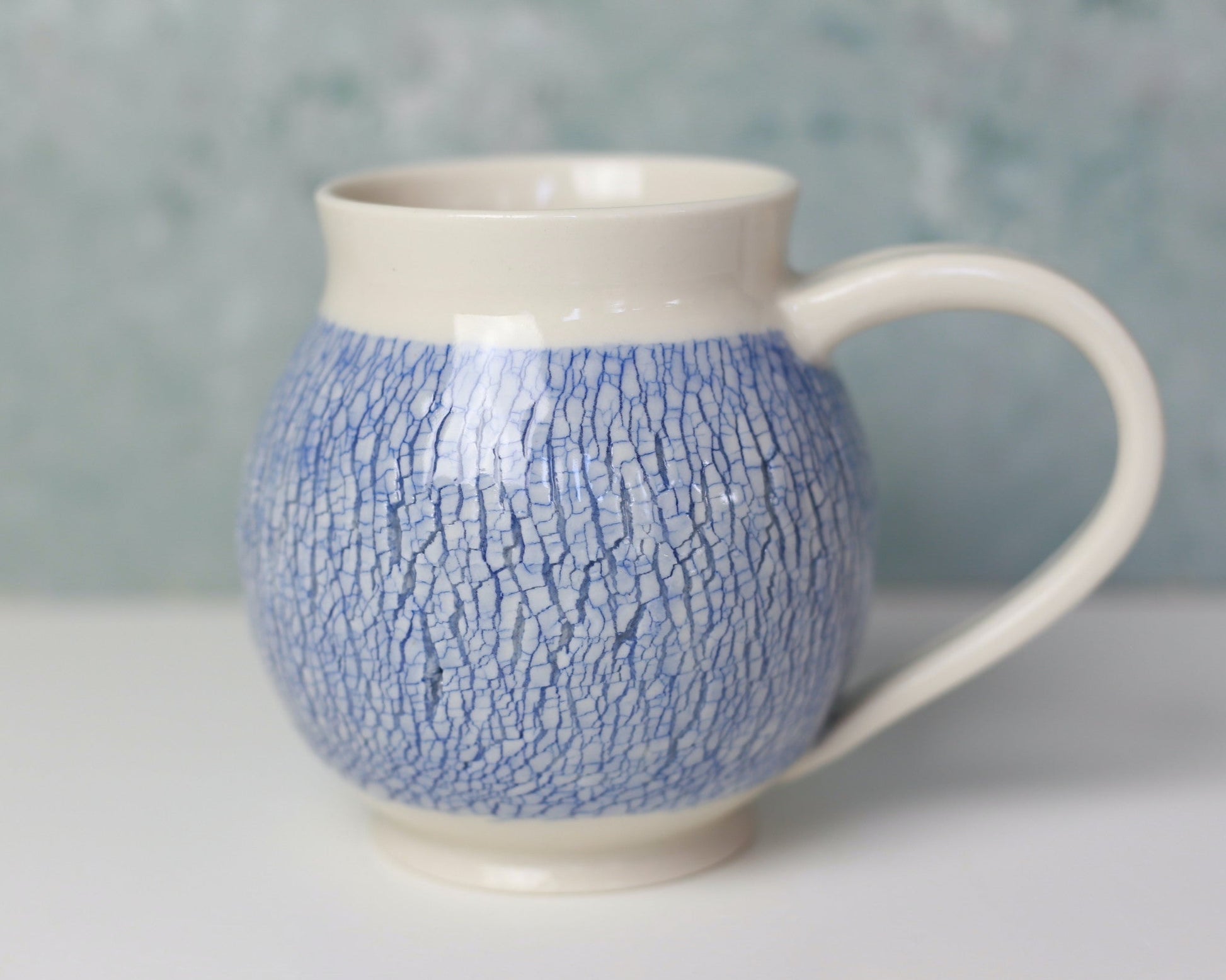 Ceramic mug with blue textured pattern on a white surface with a gray background