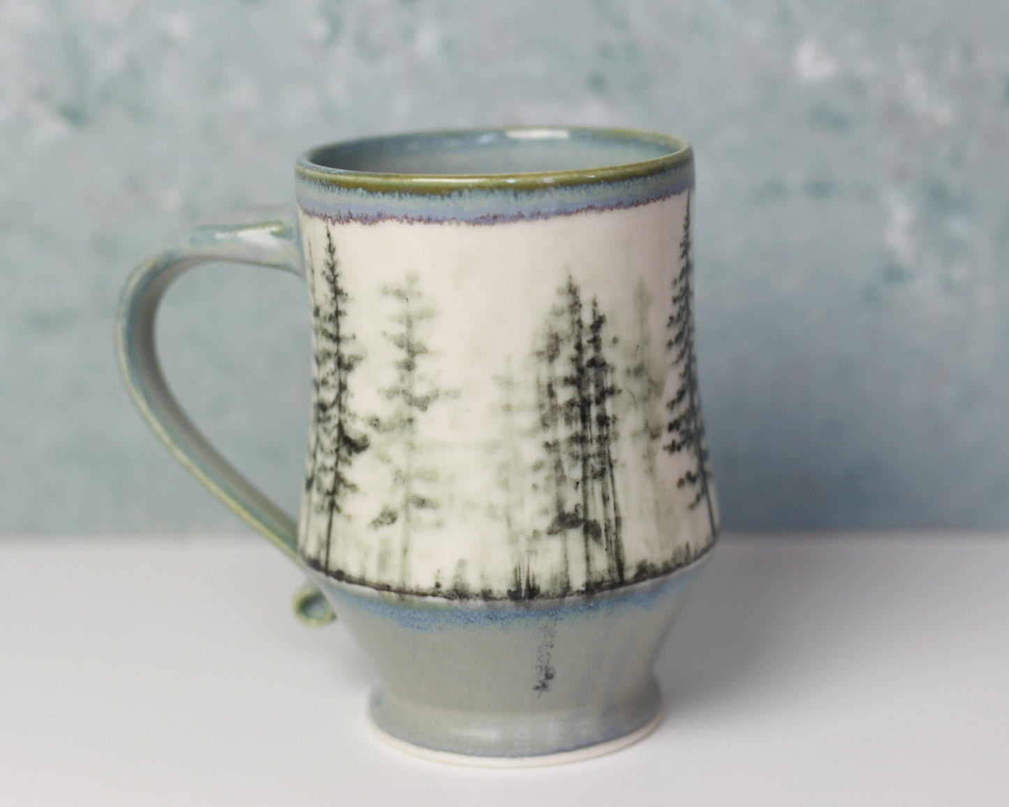 Ceramic mug with tree design on a white surface and gray background
