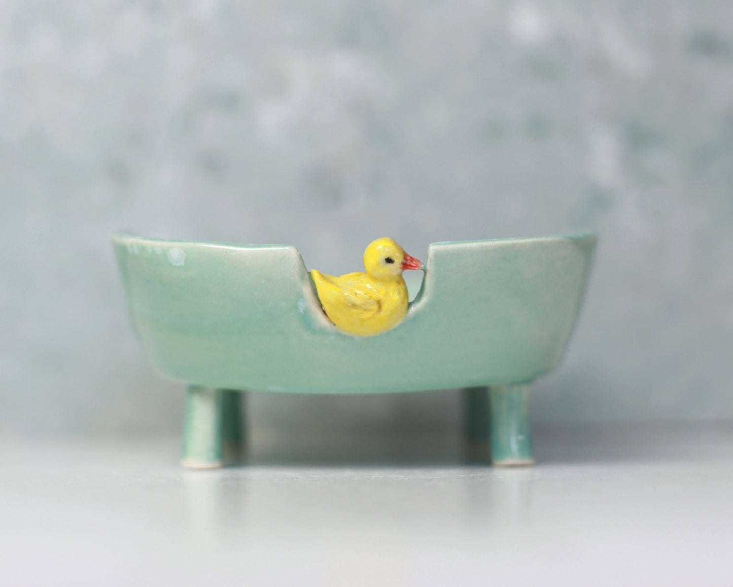 Small ceramic bathtub soap dish with a yellow duck on a light gray background