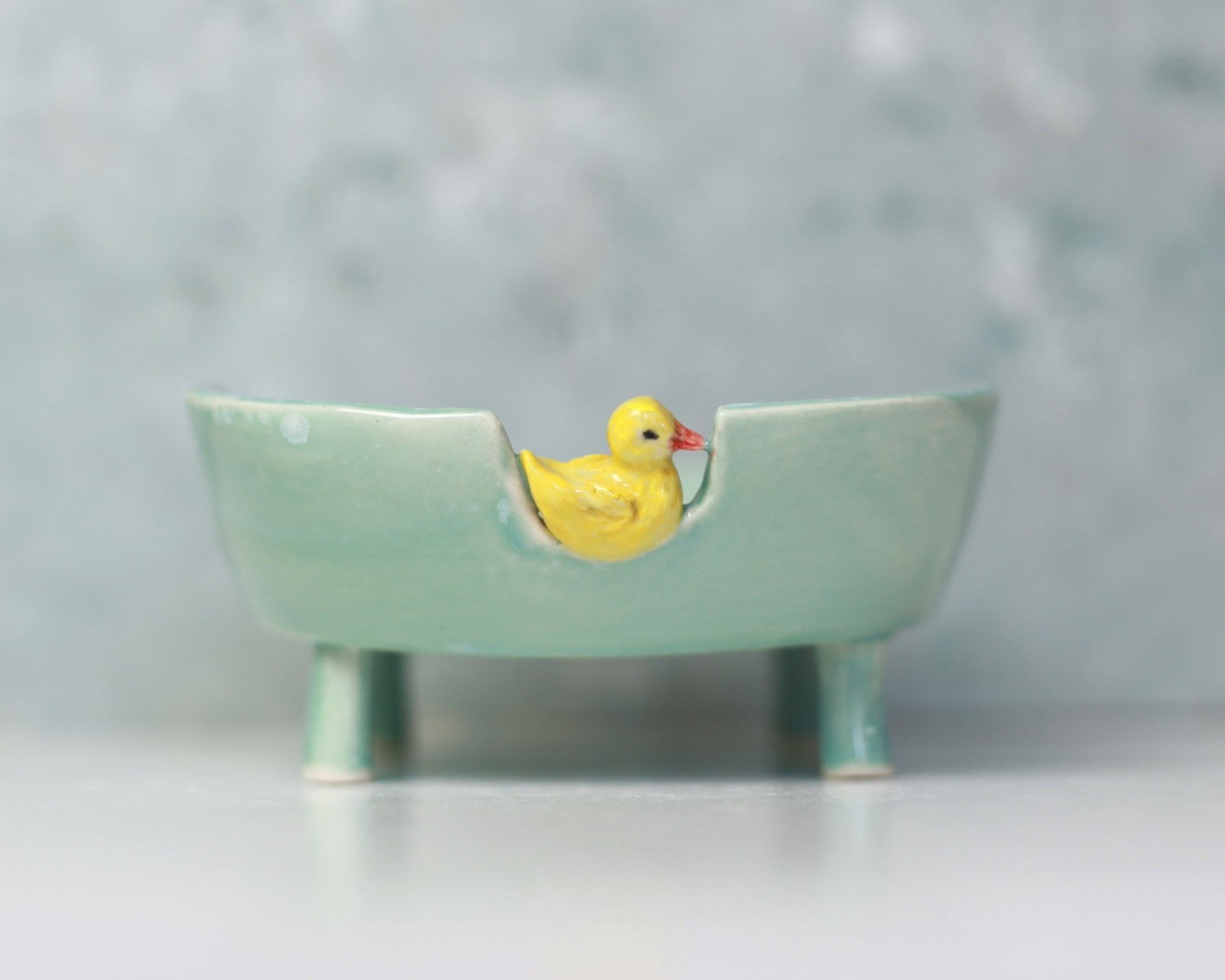 Small ceramic bathtub soap dish with a yellow duck on a light gray background