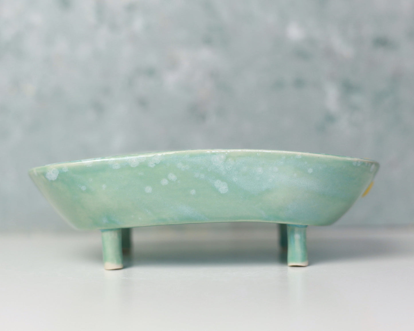 Green ceramic soap dish on a white surface with a gray background