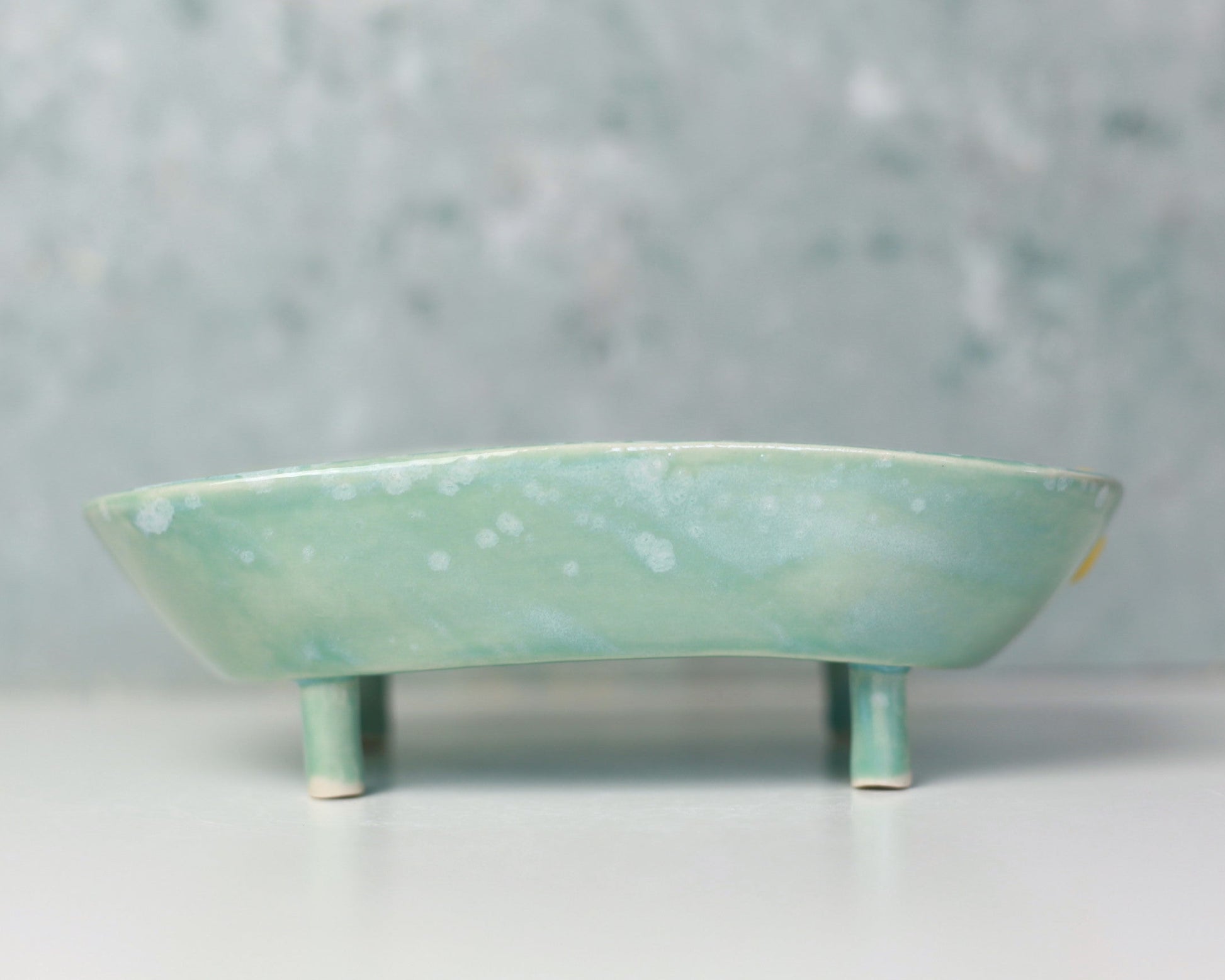 Green ceramic soap dish on a white surface with a gray background