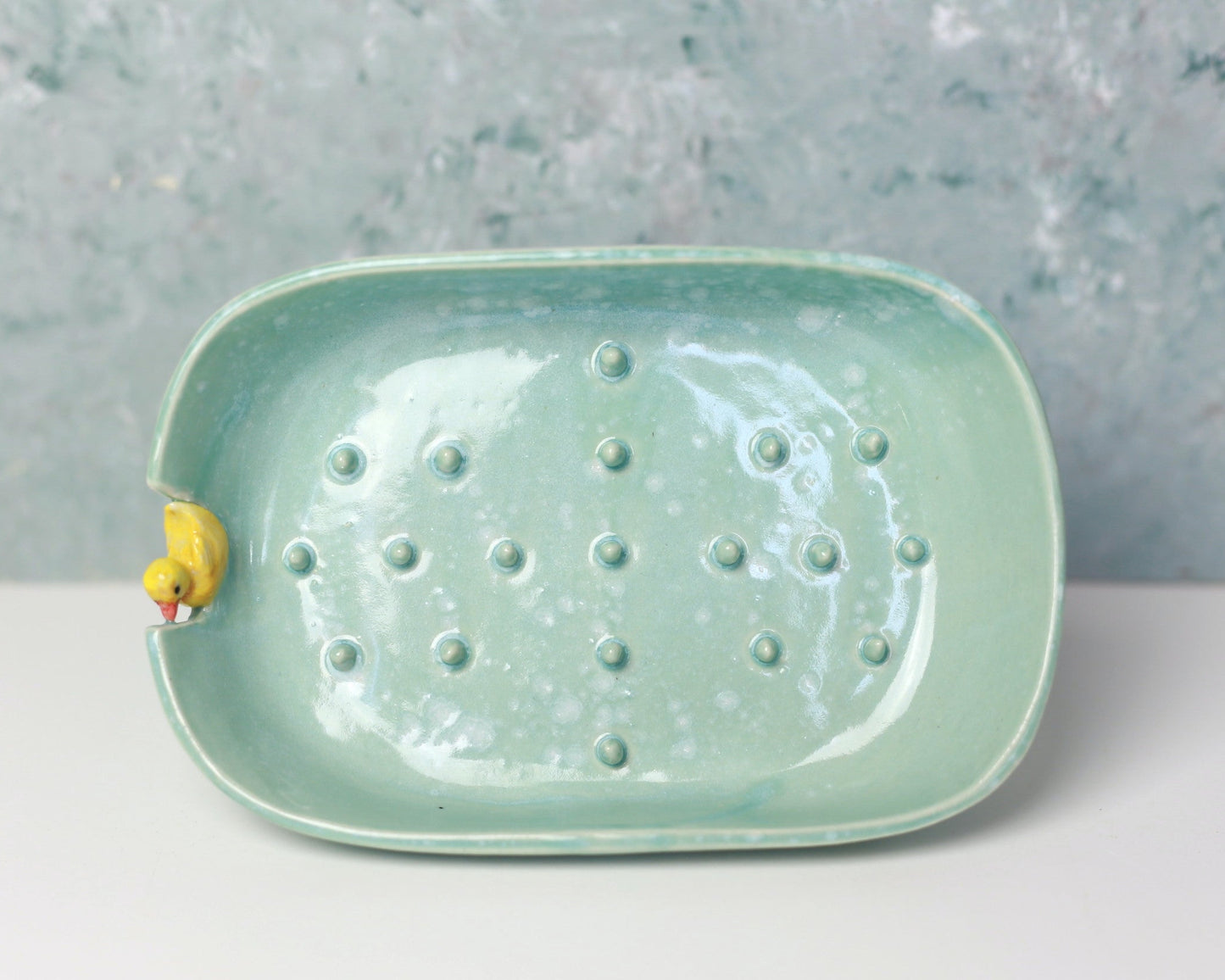 Green ceramic dish with textured surface and small yellow duck figure on a gray background