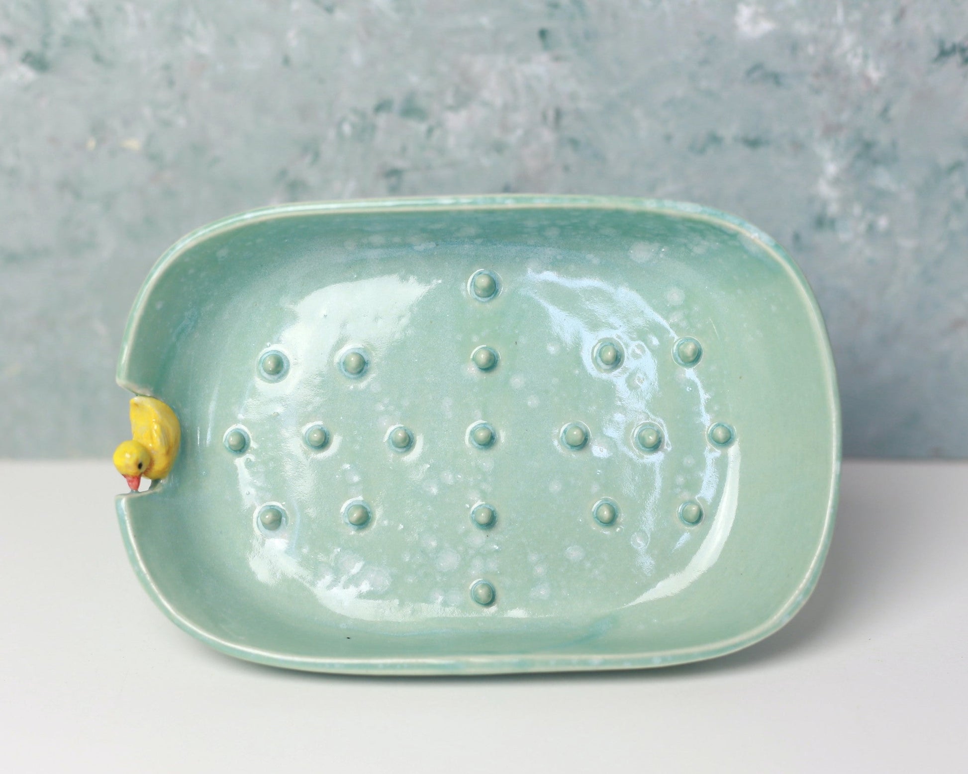 Green ceramic dish with textured surface and small yellow duck figure on a gray background