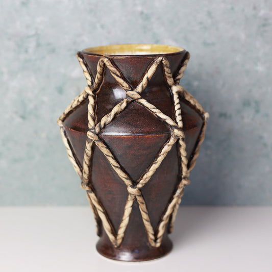 Brown ceramic vase with rope design on a gray background