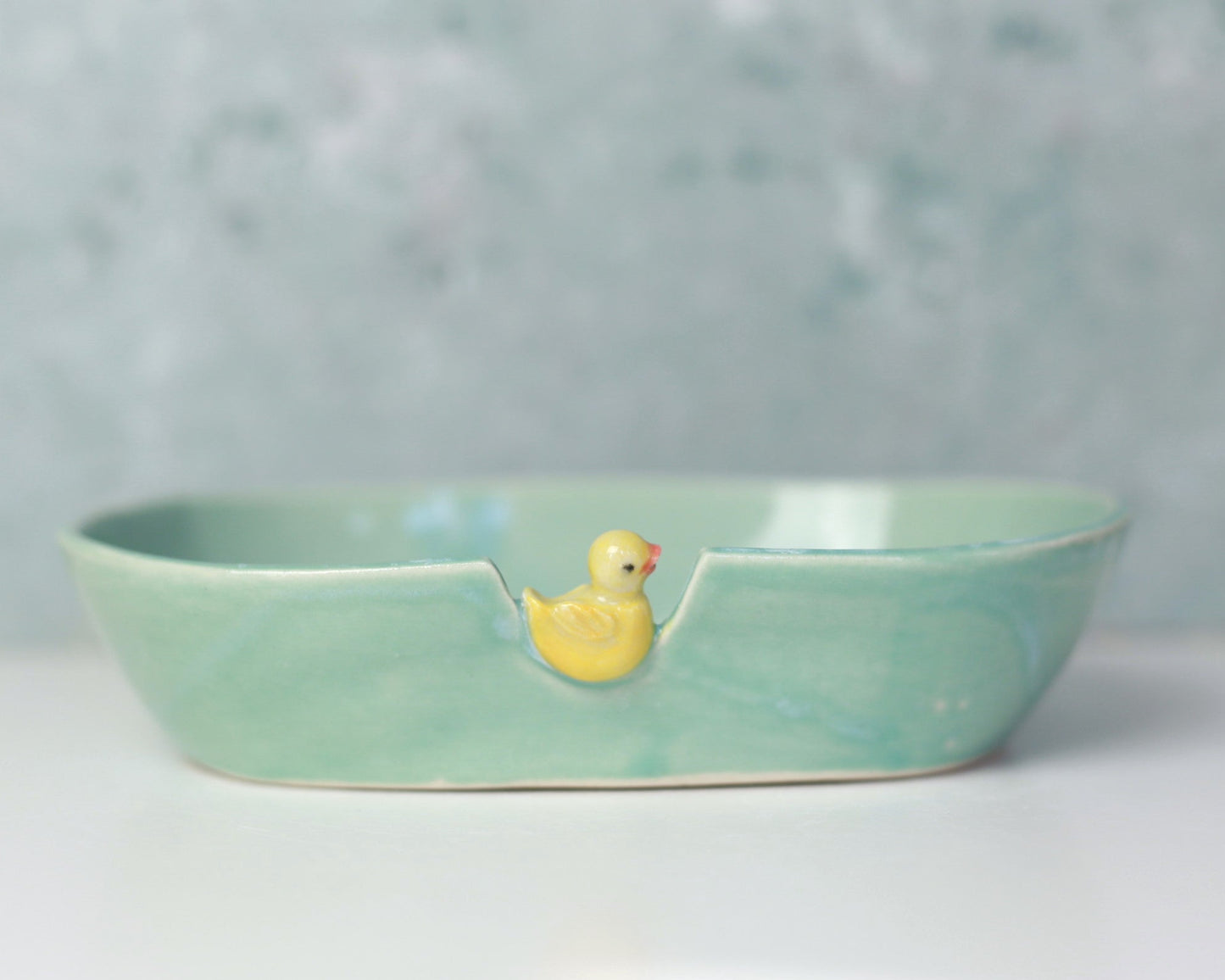 Green ceramic soap dish with a yellow rubber duck on a light gray background