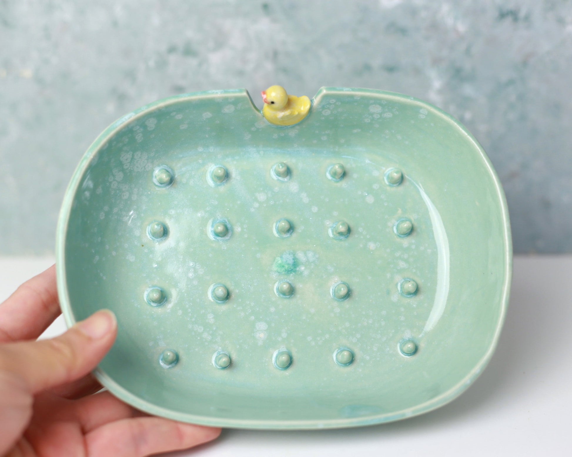 Green ceramic dish with textured surface and small yellow duck figure on a light gray background