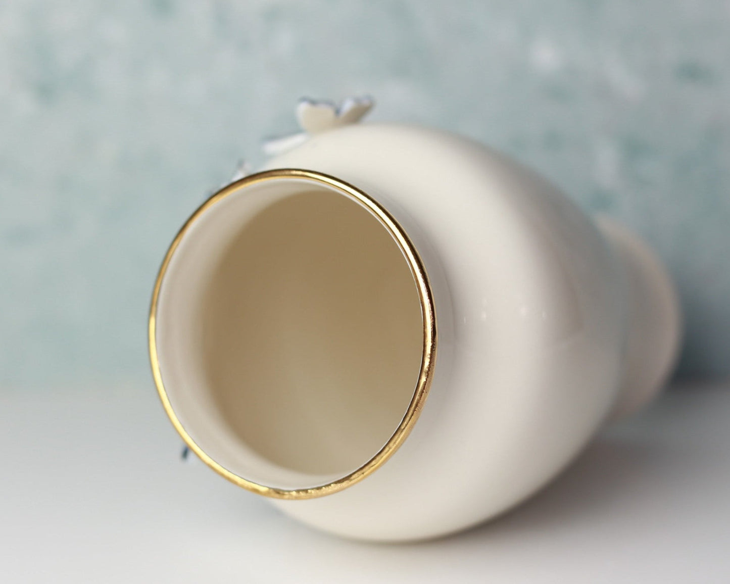 White ceramic vase with gold rim on a light blue background