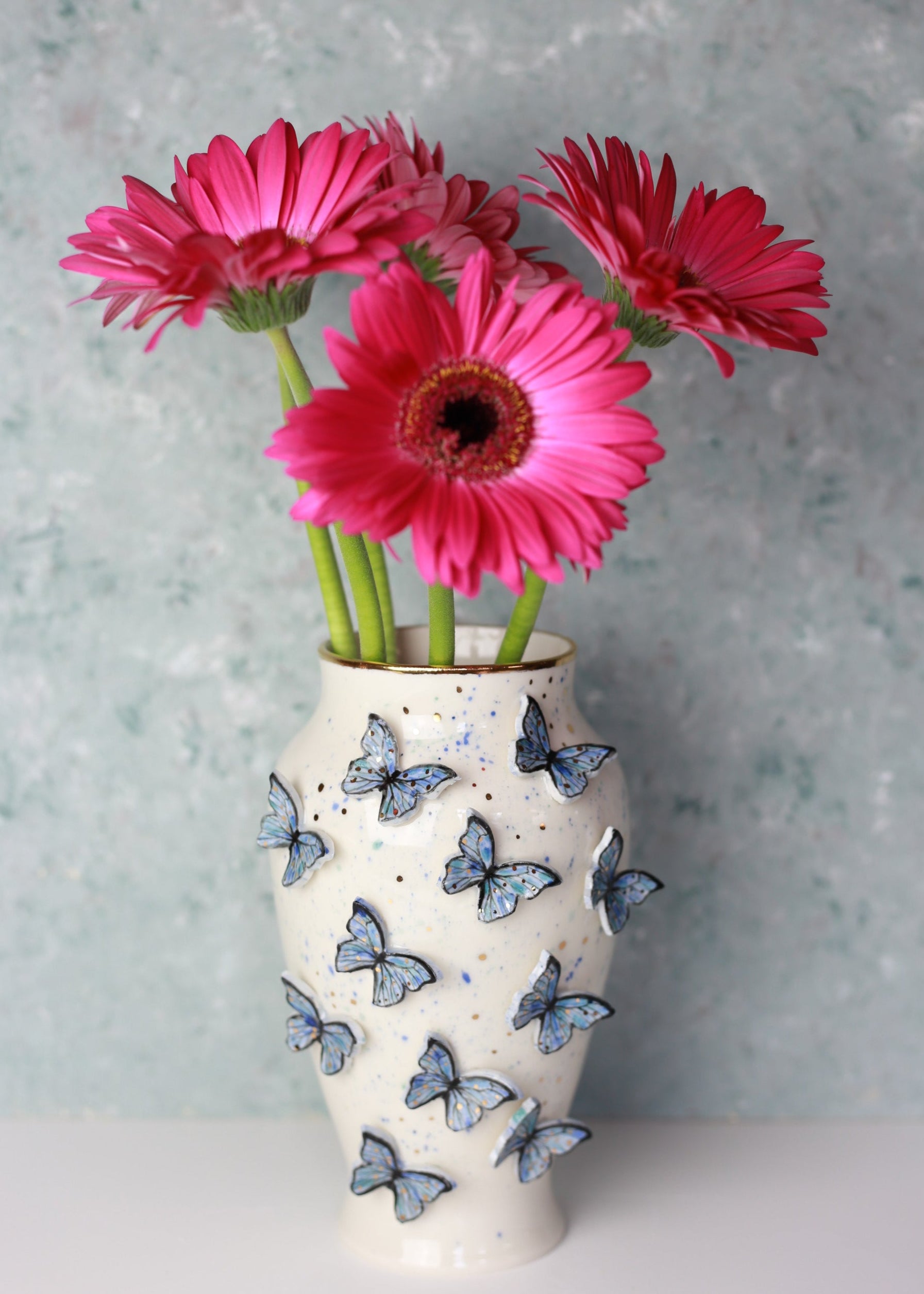 Decorative vase with pink flowers and butterfly designs on a light gray background