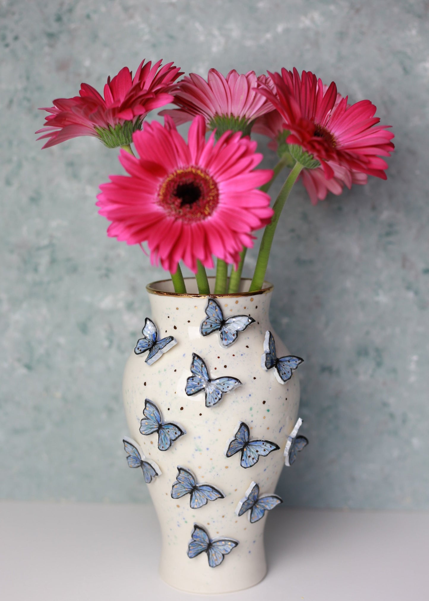 Decorative vase with butterfly patterns holding pink flowers against a gray background