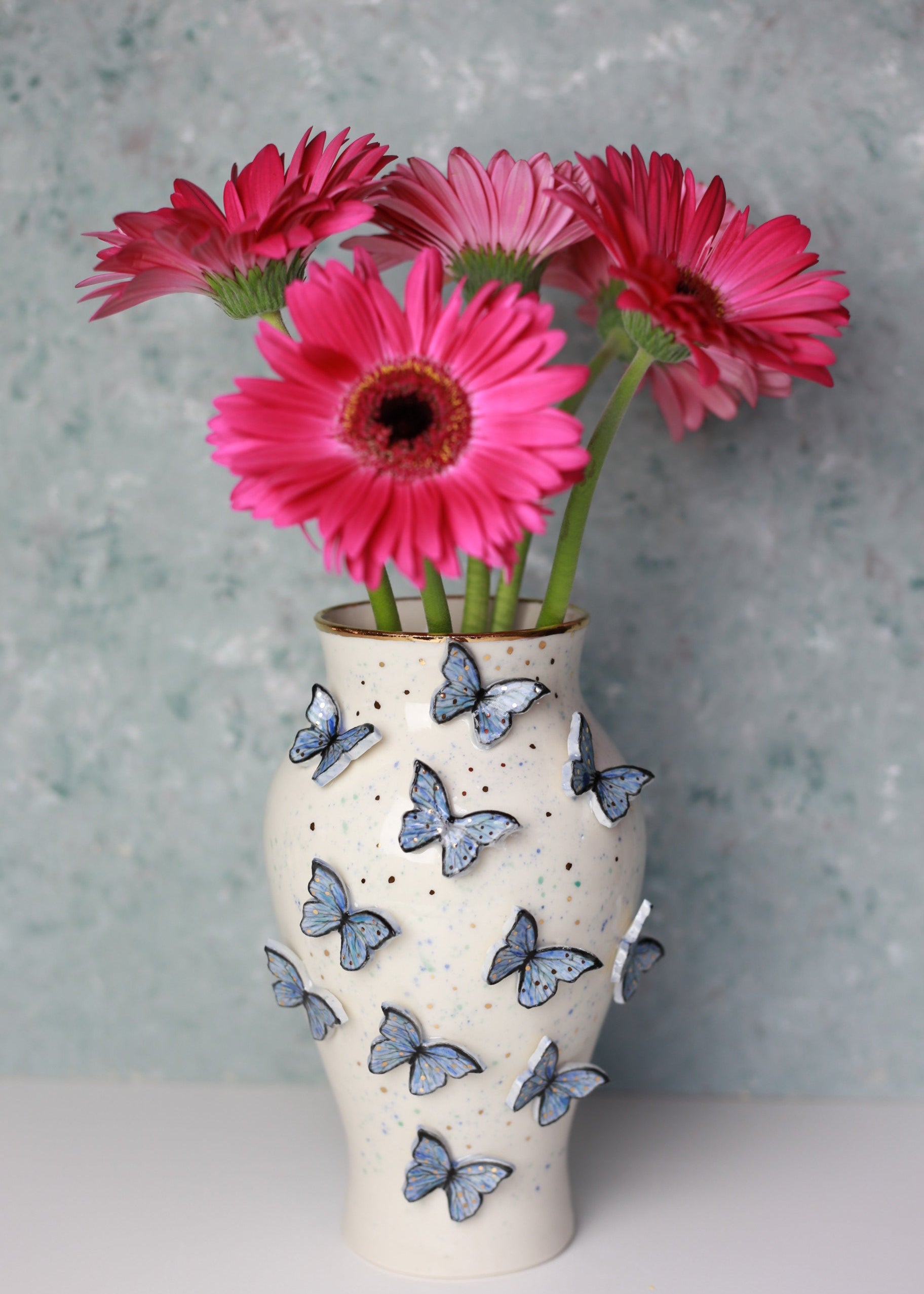 Decorative vase with butterfly patterns holding pink flowers against a gray background