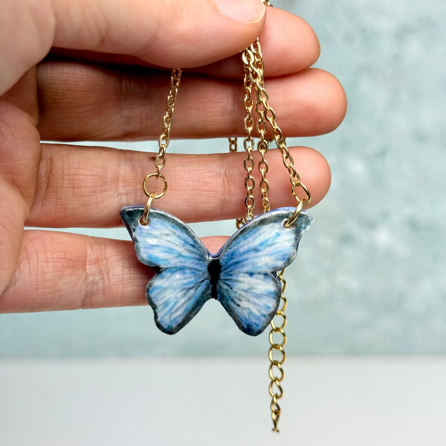 Butterfly necklace held by a hand with a blurred background