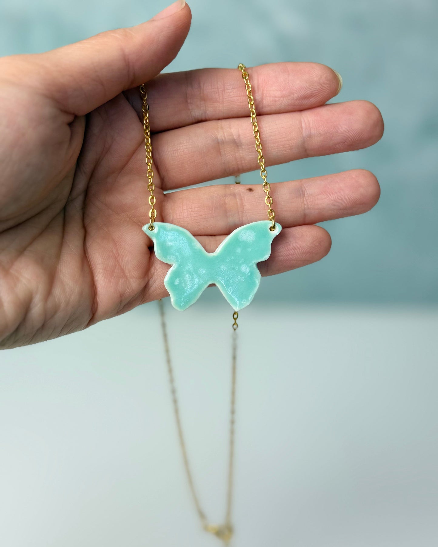 Hand holding a necklace with a butterfly pendant against a light background